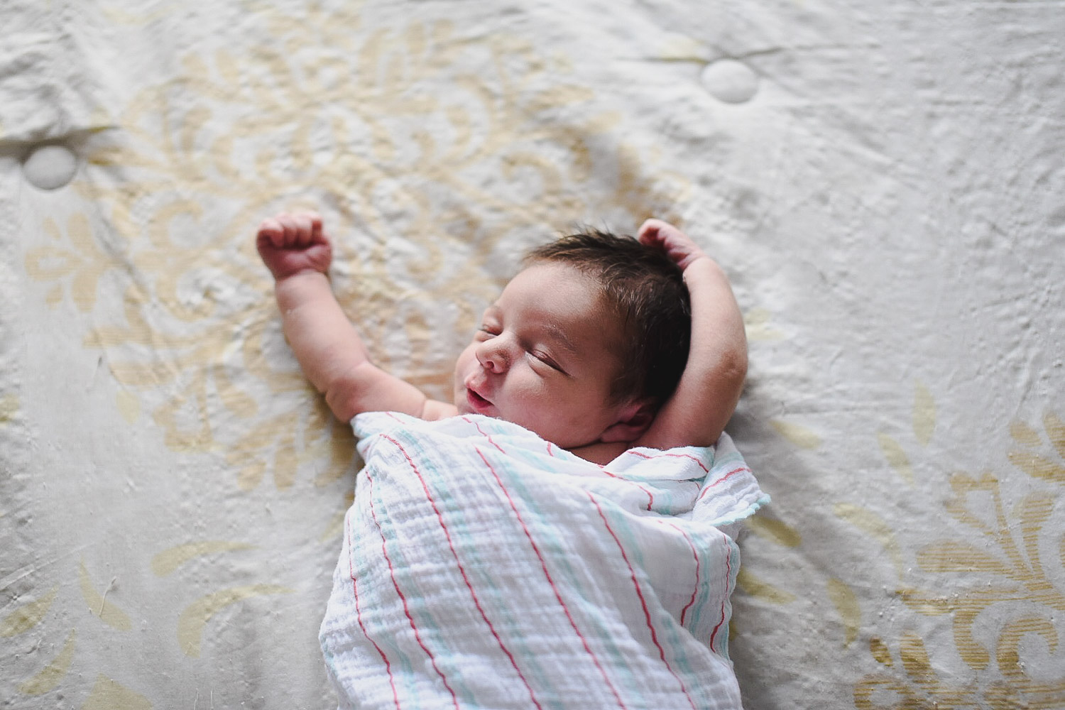 Baby in a swaddle blanket with arms up. What baby items do you really need?